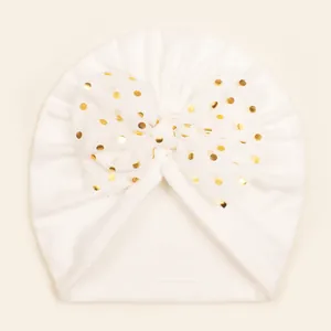 Detail of white baby beanie with a large gold polka dot mesh bow decoration