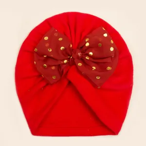 Close-up of red knit baby hat with large gold polka dot tulle bow detail