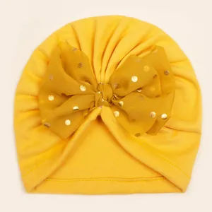 Detail of baby turban hat showing ginger yellow knit fabric and golden dot mesh bow