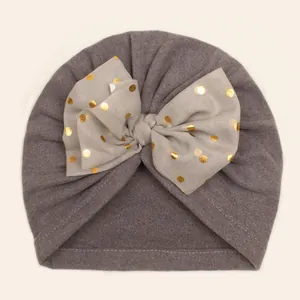 Detail of baby turban hat with double layer bow and gold polka dot print on soft grey fabric