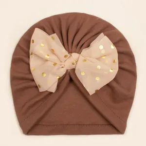 Detail of baby turban hat featuring a golden polka dot mesh bow on soft brown fabric
