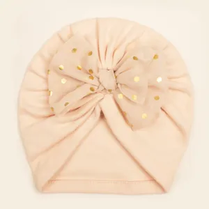Close-up of baby turban hat featuring a large gold polka dot sheer tulle bow detail