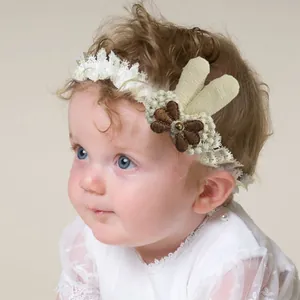 Lace baby headband with crochet flower and rabbit ears on infant model in soft white color