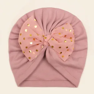 Detail of baby warm hat with a large pink organza bow and golden foil polka dots