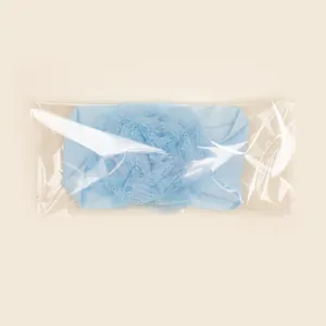 Detail van de lichtblauwe baby haarband van nylon met bloem in transparante verpakking