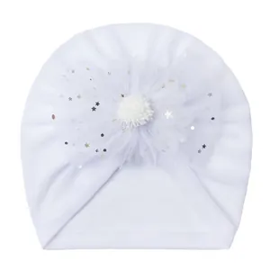 Detail of white infant turban hat with mesh flower, sequins, and plush pompom