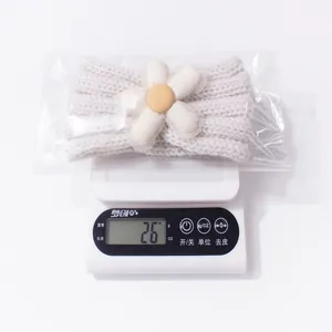 Detail of light beige knitted baby headband with fabric flower being weighed at 2.6g