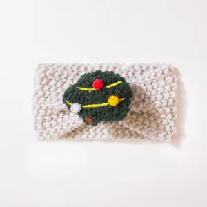 Detail eines gestrickten Baby-Stirnbands mit beiger Wolltextur und grünem Bommel-Dekor