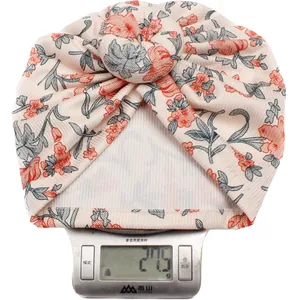 Nahaufnahme einer leichten Baby-Turbanmütze mit Blumenmuster auf einer Waage mit 27,5g