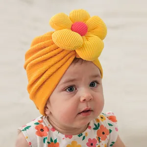 Détail d'un bonnet turban pour bébé orange en maille avec une grande fleur 3D colorée