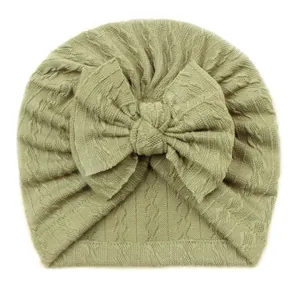 Gros plan détaillé du bonnet turban tricoté vert sauge pour bébé avec un grand nœud
