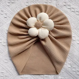 Détail du turban pour bébé avec texture gaufrée et grand élément décoratif floral blanc