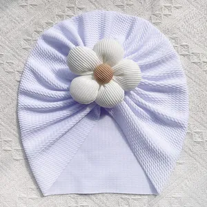 Détail du bonnet turban blanc pour bébé avec texture tricotée et grande fleur 3D centrale