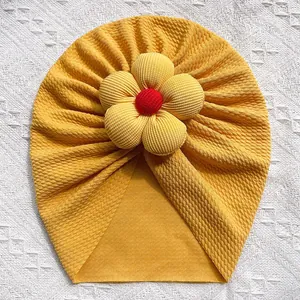 Détail d'un bonnet turban jaune pour bébé avec texture gaufrée et grande fleur en 3D
