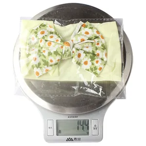 Bandeau bébé avec nœud à motif marguerite sur une balance numérique affichant 14,4g