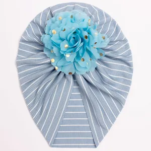 Close-up of baby turban hat featuring blue striped knit and gold polka dot flower detail