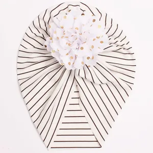 Detail of baby striped turban hat featuring a large white mesh flower with gold polka dots
