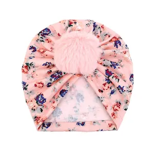 Détail d'un bonnet turban rose à fleurs pour bébé avec un grand pompon en peluche