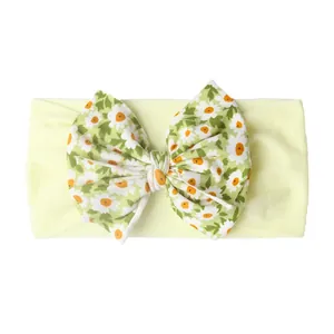 Détail d'un bandeau bébé avec un grand nœud jaune à motif marguerites sur tissu élastique