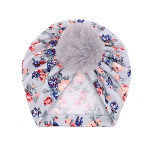 Détail du bonnet turban pour bébé avec motif floral rouge et grand pompon en fausse fourrure