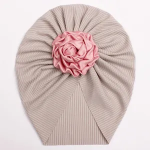 Macro detail of ribbed knit infant turban hat featuring a large pink satin rose flower decoration