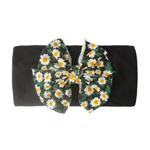Détail d'un bandeau bébé avec un grand nœud imprimé marguerites sur tissu noir
