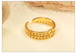 Détail macro d'une bague ouverte dorée 18K à double chaîne sur fond de pierre