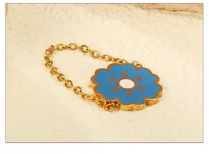 Macro shot of blue floral enamel charm on a gold link chain ring over stone texture