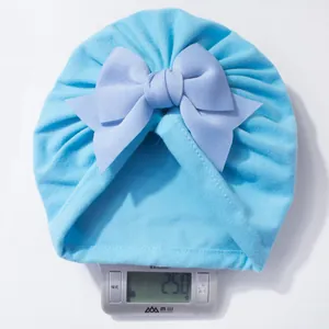Détail d'un bonnet bébé bleu ciel avec nœud, pesant 25,0g sur une balance précise