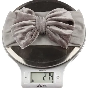 Detail shot of a grey velvet baby headband weighing 21.4g on a digital scale