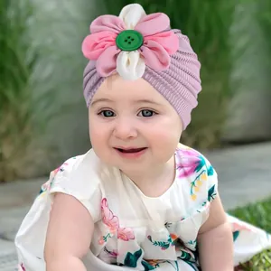 Détail d'un turban pour bébé orné d'une grande fleur en mousseline et bouton vintage