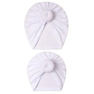 Close-up of set of two white knit baby turban hats with donut knot and soft ribbed texture