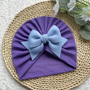 Détail d'un turban pour bébé avec plis violets et un grand nœud bleu clair décoratif