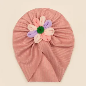 Détail d'un bonnet turban rose côtelé pour bébé avec fleur en tissu colorée et bouton vert