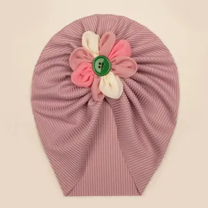 Détail d'un turban pour bébé avec une fleur en tissu tricolore faite main et un bouton