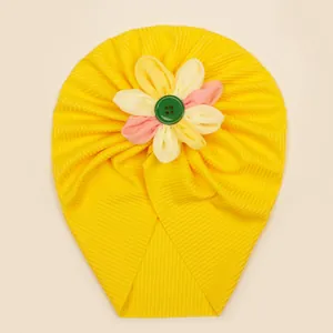 Détail du turban pour bébé en tricot jaune avec une grande fleur tricolore et bouton