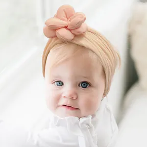 Gros plan d'un bébé portant un bandeau en nylon rose saumon avec fleur 3D artisanale
