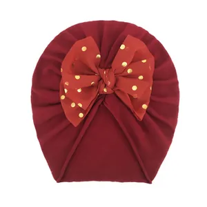 Dunkelrote Baby-Turbanmütze mit großer goldener Punkte-Chiffonschleife auf weißem Grund
