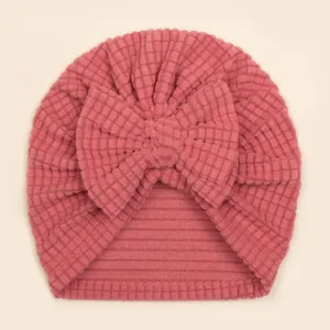 Detail einer rosa Waffelstrick-Babymütze mit großer Schleife und Rippenstricksaum
