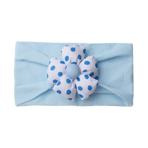 Detail of baby headband with a large blue polka dot fabric flower on soft fabric