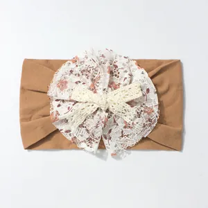 Detail of baby headband with brown elastic fabric and floral white lace bow accessory