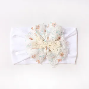 Close-up of white baby headband featuring lace floral patterns and a crochet bow detail