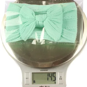 Macro shot of 14.5g light green nylon baby bow headband being weighed on a digital scale