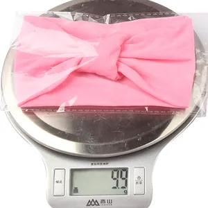 Pink knotted nylon baby headband weighing 9.9g on a digital scale for size reference