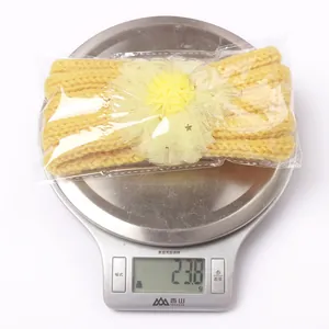 Bandeau tricoté jaune pour bébé avec fleur en maille placé sur une balance