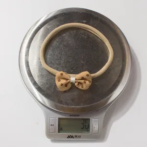 Detail shot of a lightweight 3.6g baby headband with floral bow on a digital scale