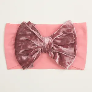 Détail d'un nœud en velours rose sur un bandeau élastique en nylon pour bébé
