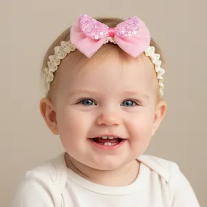 Dettaglio del fiocco rosa con paillettes su fascia per neonata in pizzo bianco