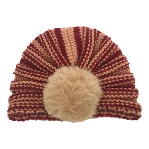 Detailed knit texture of striped baby beanie featuring a large fluffy faux fur pompom