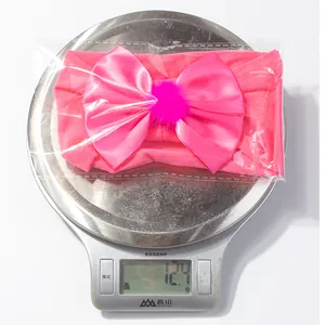 Close-up of pink nylon baby headband with bow and pompom on a scale weighing 12.4g